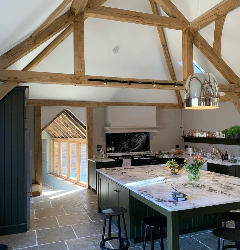 An oak-framed barn kitchen wired by Saltdean Electrical: track lighting along the beam, a polished pendant over a long marble island, flagstone floor