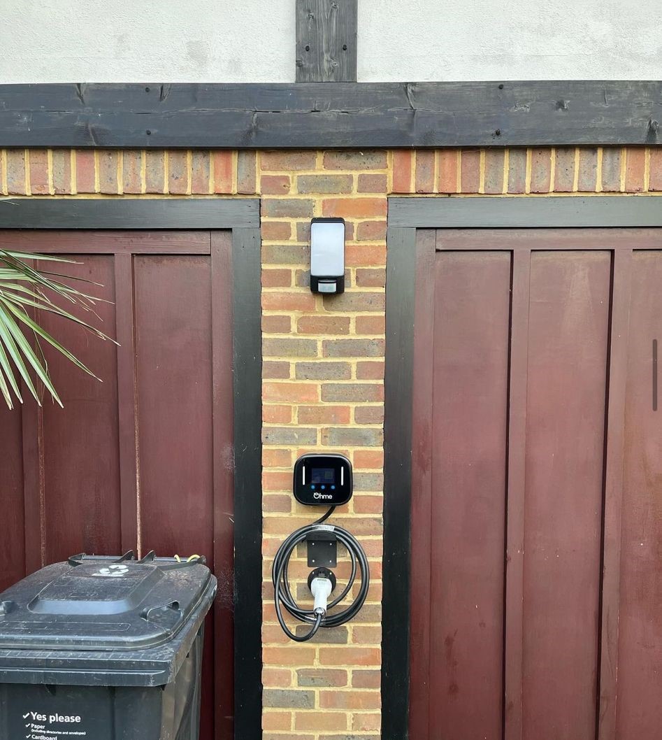 Wall-mounted EV charger with its cable coiled, on a brick wall beside a garage door