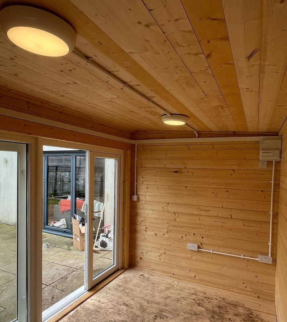 Pine-clad garden room with ceiling lights, a wall-mounted consumer unit and surface conduit
