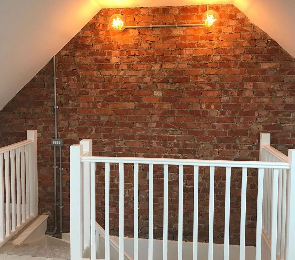 Exposed brick wall on a stair landing with a twin industrial-style wall light